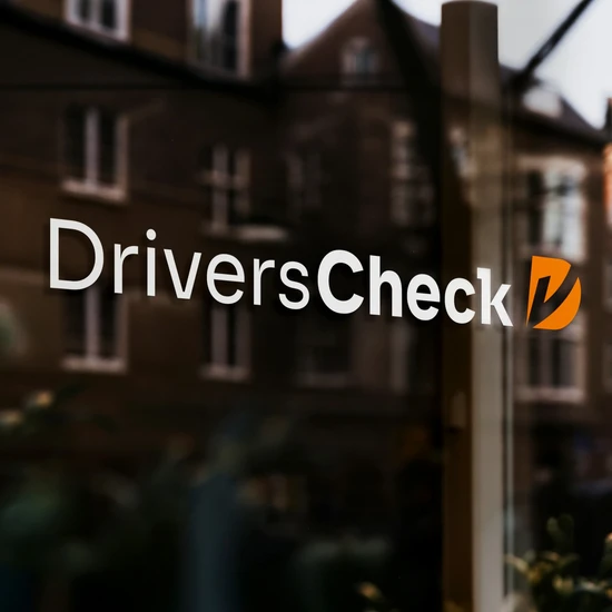 Redesign der Wort-Bild-Marke von DriversCheck Fensterscheibe mit dem neuen DriversCheck Logo in der sich das gegenüberliegende Haus spiegelt