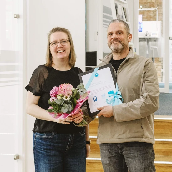 Fief Johr ist Levke dor Zwei Personen lächeln in die Kamera, die Frau trägt einen Blumenstrauß in der Hand und der Mann eine Urkunde