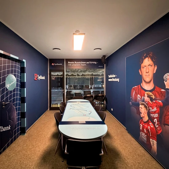 Neugestaltung derSG Loge für dieAL Sydbank Blick in eine SG Loge der Sydbank, mit einem Tisch und Stühlen, sowie Blick auf das Handballfeld