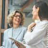 Zwei Frauen in schicker Kleidung lachen sich an.